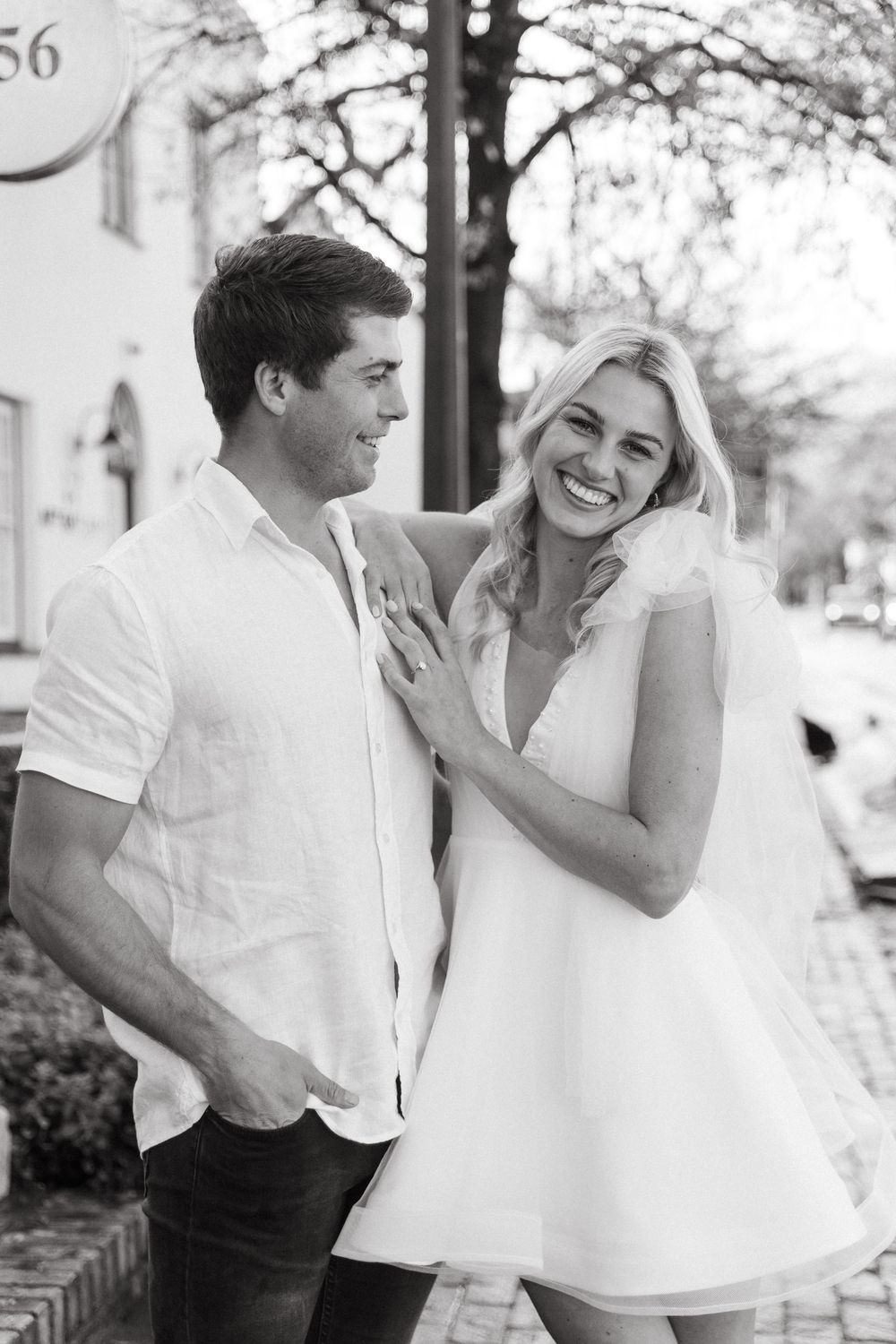 Two joyful individuals in white attire share affectionate moments in a series of black and white outdoor photographs.