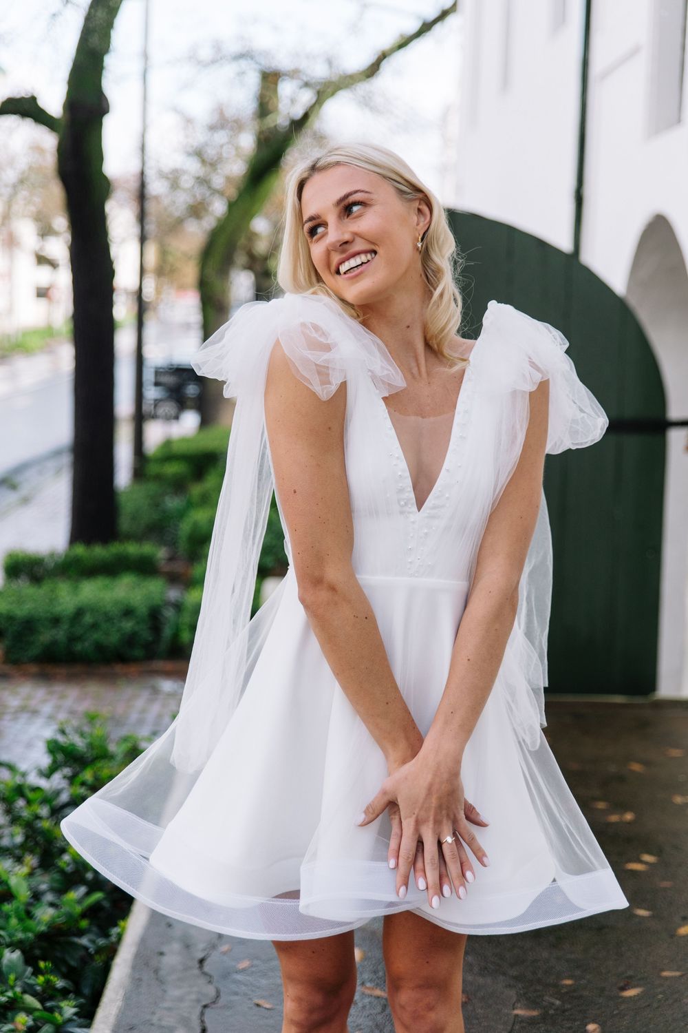 A joyful moment captured in white attire against a classic architectural backdrop with greenery.