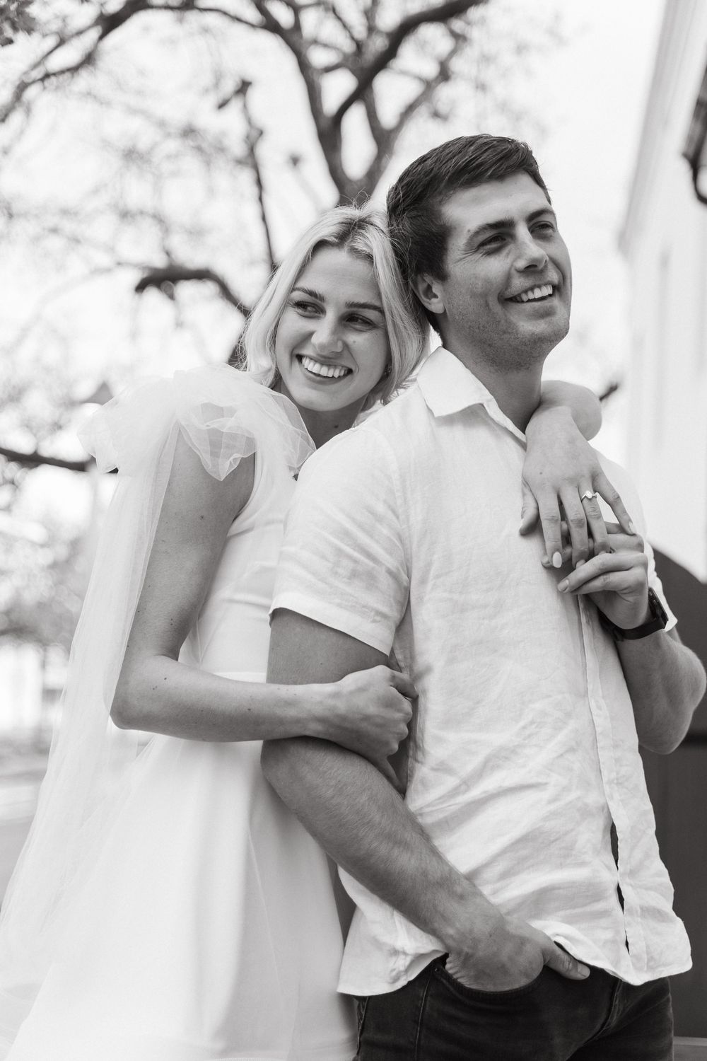Candid black and white photos capture tender moments between two people wearing white outdoors.