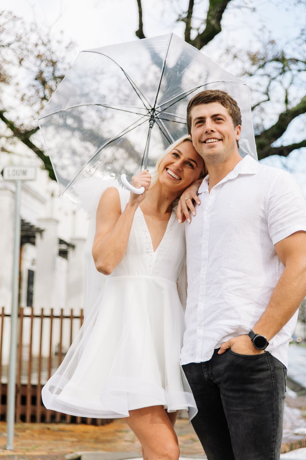 A couple in white shirts share a joyful moment under blooming cherry blossom trees.