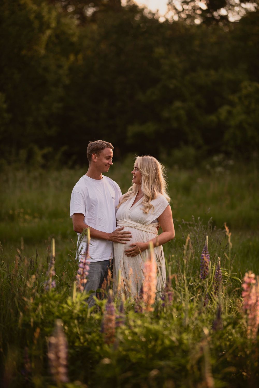 Couple sharing intimate moment among blooming lupine flowers in a meadow at dusk.