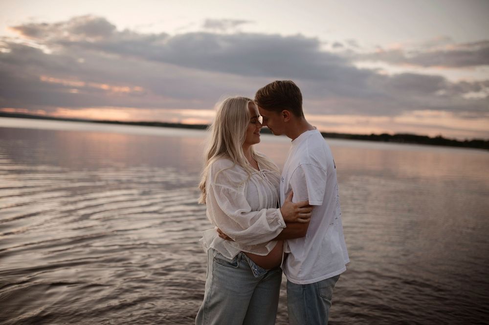 A tender moment between two people standing in shallow water at dusk with a peaceful lake backdrop.