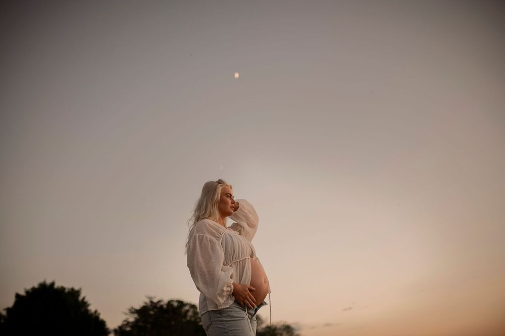 A couple shares an intimate moment at dusk with a dreamy, warm-toned sky and moon in the background.
