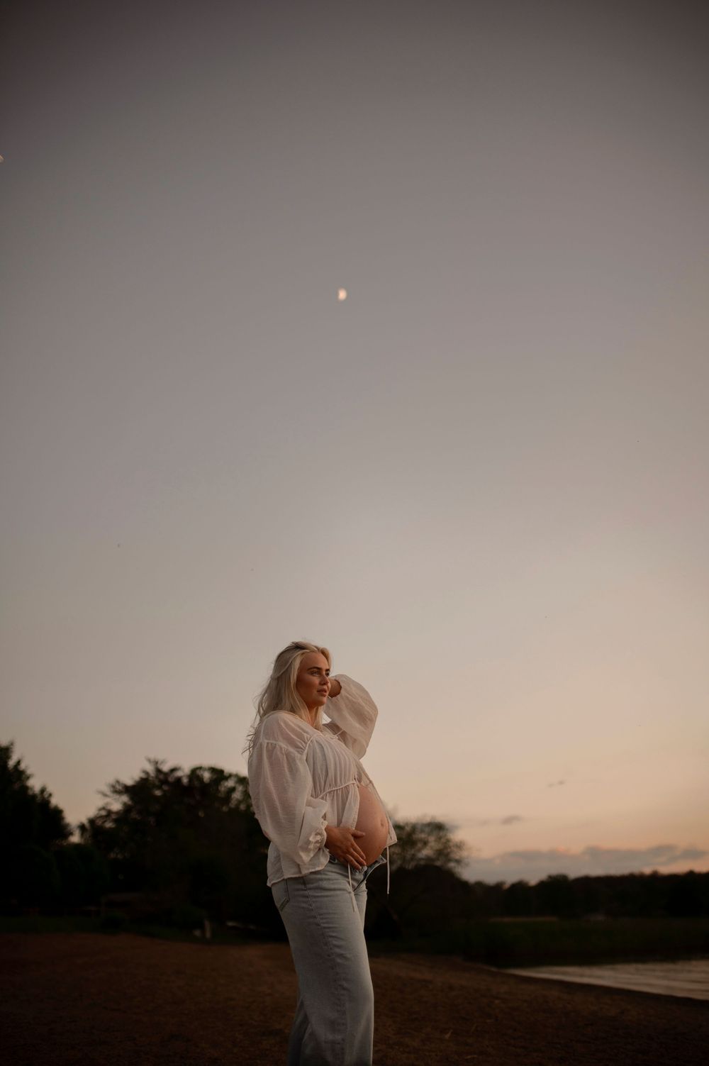 A couple embraces tenderly in silhouette against a dusky sunset sky on a grassy hilltop.