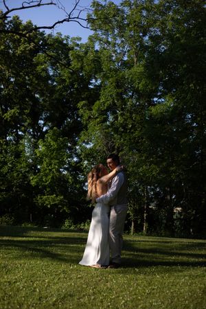 A romantic outdoor scene between two people in white attire against a tree-lined backdrop.