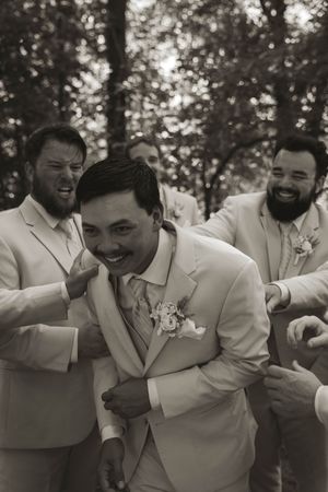 Groomsmen in light colored suits share a candid laughing moment.