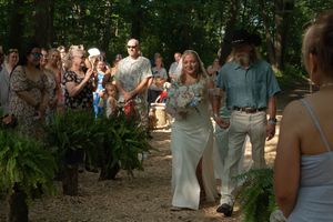 Wedding guests gather in a wooded area for an outdoor ceremony.