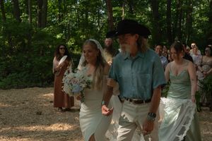 Wedding attendees stand in a forest clearing during a summer ceremony.