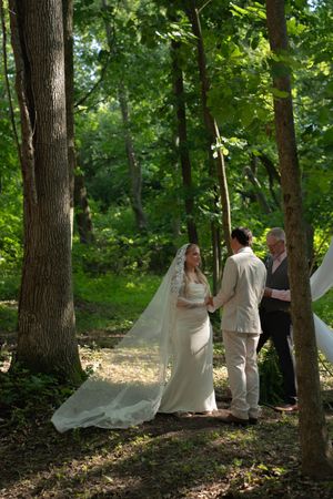 A wedding ceremony unfolds in a serene forest setting with dramatic lighting.