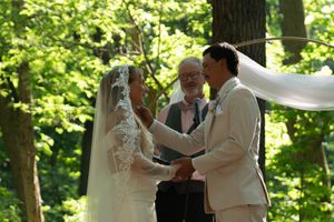 Wedding party members gather under tall trees for outdoor ceremony photos.