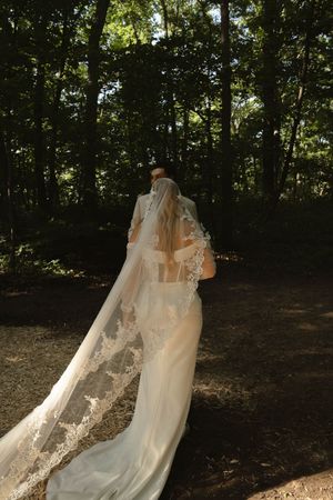 A flowing white wedding veil catches sunlight in a wooded outdoor setting.