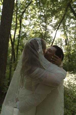 A tender wedding embrace captured in a forest with sunlight filtering through trees.