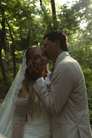 A romantic kiss between newlyweds in a sunlit forest setting.