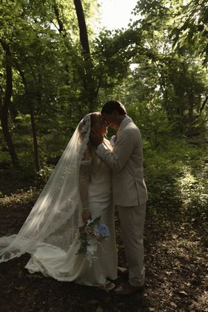 A couple embraces during their woodland wedding ceremony with a flowing veil.