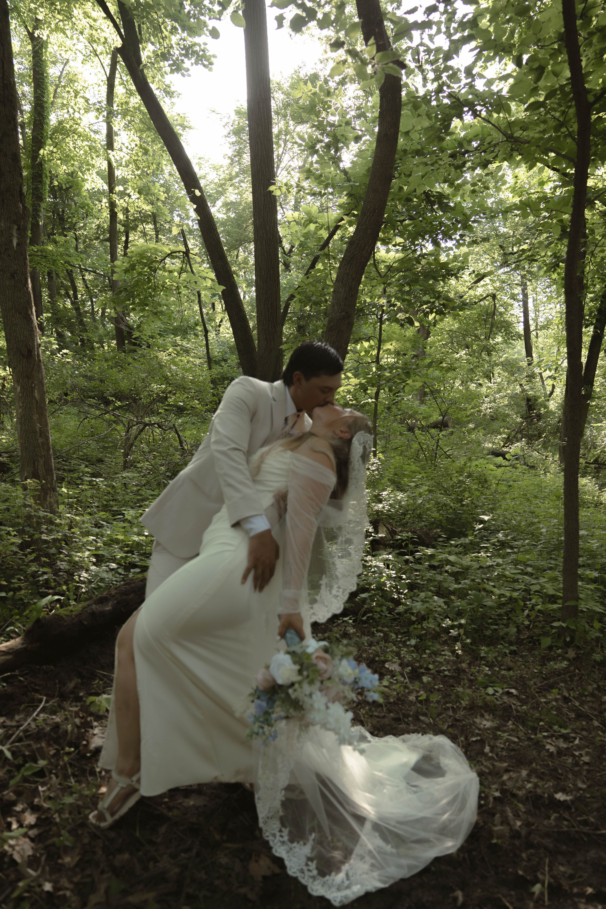 A romantic scene unfolds in a sunlit forest with flowing white dress details.