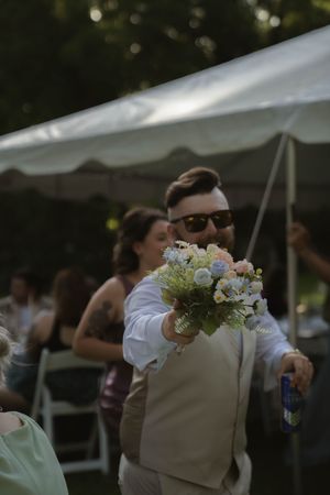 Wedding guests gather under white tents during an outdoor reception celebration.
