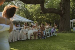 Wedding guests enjoy the outdoor reception under trees with white tents and tables visible.