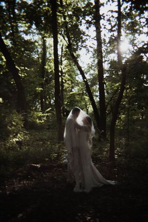 Ethereal wedding photograph in a sunlit forest with flowing white dress and veil.