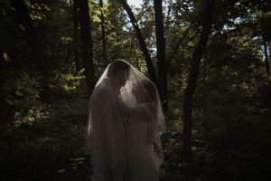 Dreamy silhouette of a wedding dress and veil captured in a mystical forest setting.