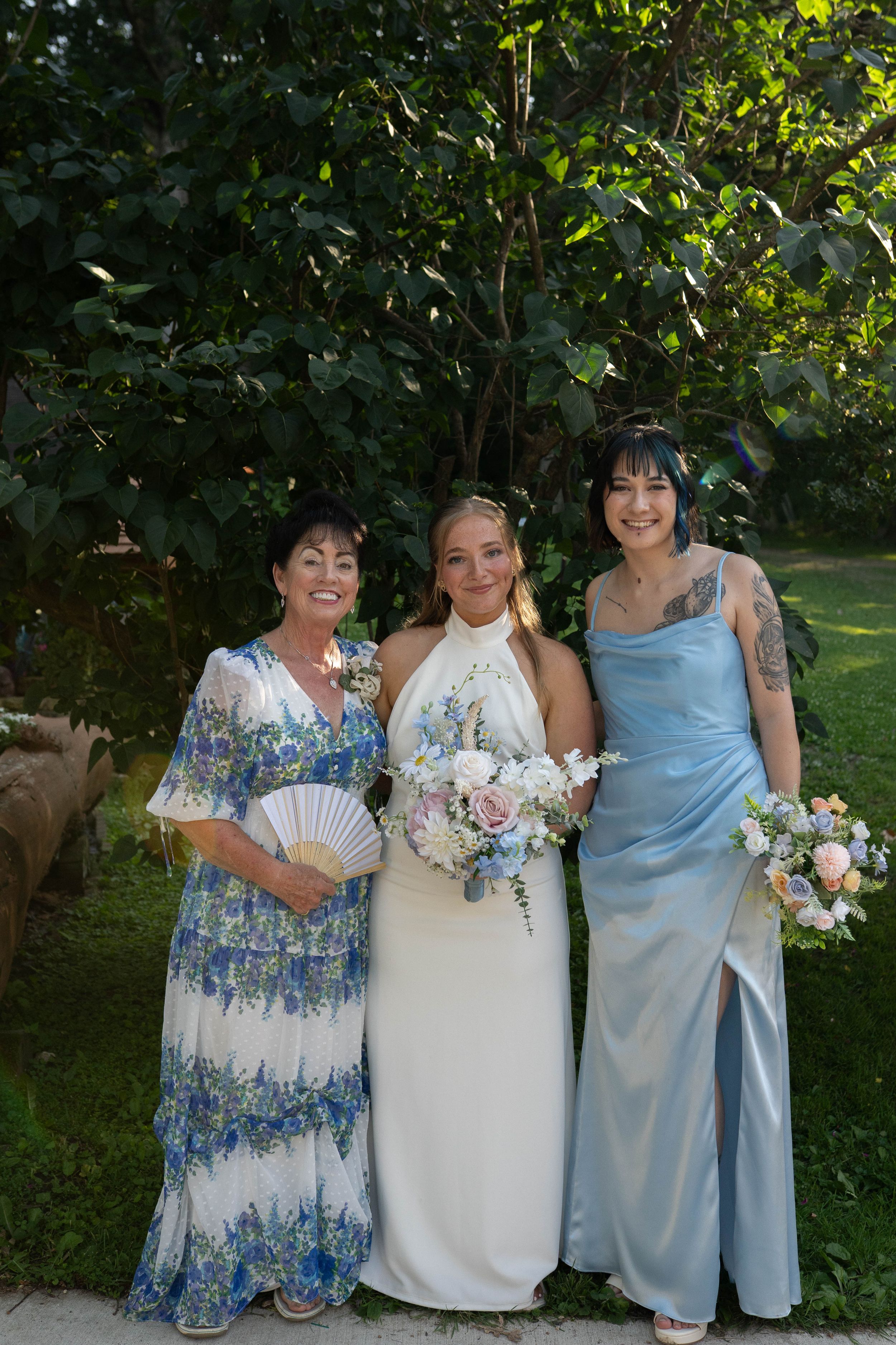 Three wedding attendees in coordinating blue and white dresses pose with floral bouquets.