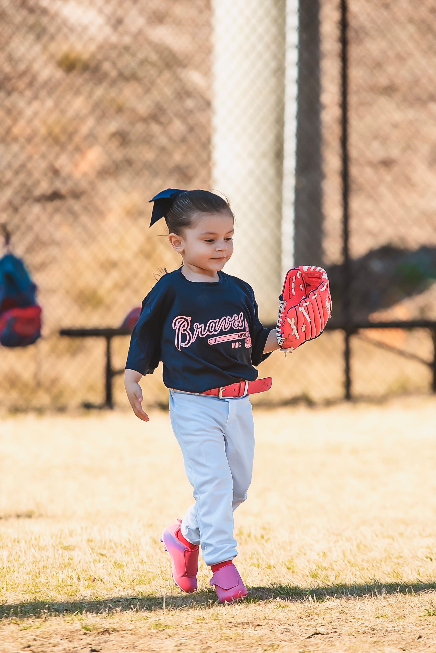 Small ballplayer in a navy Braves jersey and white pants runs through a sunlit baseball field in training.