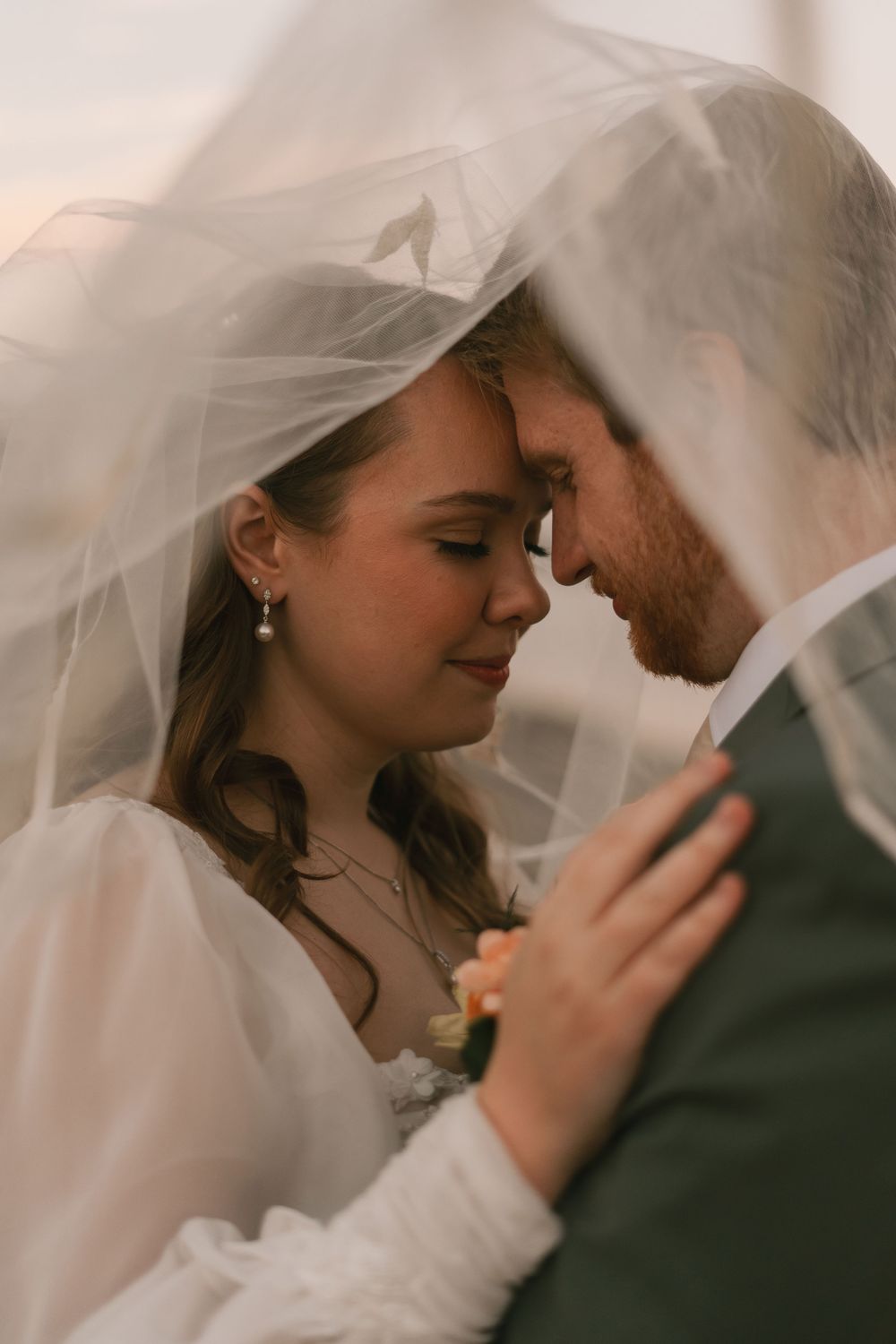 Close up view of a bride and groom under a flowing white veil captured in an intimate romantic moment.