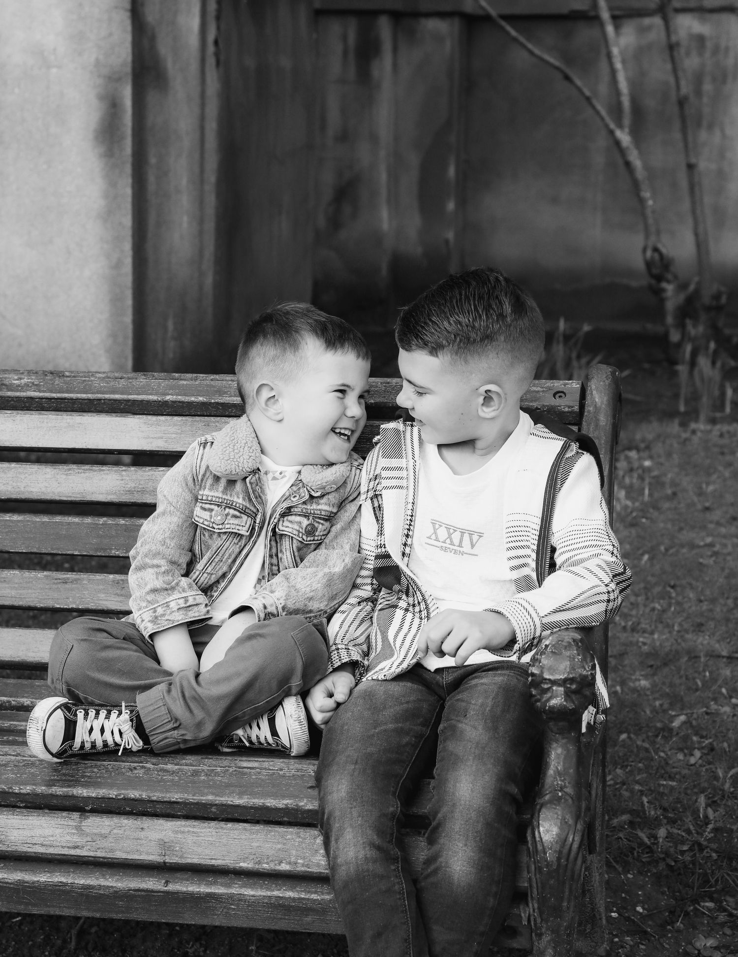 Black and white photos showing two young brothers sitting on a bench laughing during family shoot in Nottingham