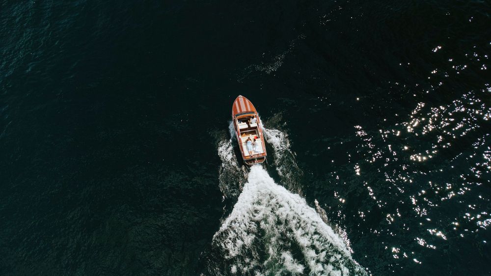 Aerial view of a small boat cutting through dark turquoise waters with a white wake trailing behind.