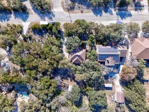 Aerial drone view of a tree-covered residential property with solar panels on the roof in a wooded Texas neighborhood.