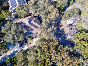 Close aerial drone view of a secluded home nestled among dense trees with a dirt driveway in Texas.