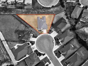 Overhead aerial drone view of a triangular residential property lot outlined in orange among suburban homes on a cul-de-sac.