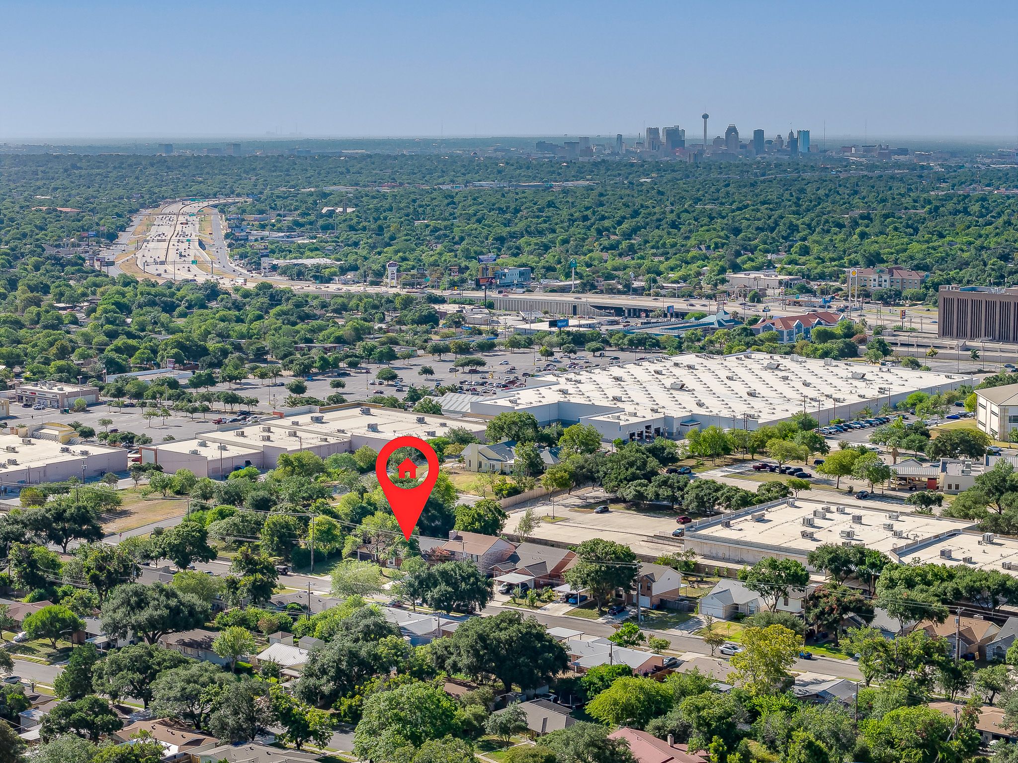 Aerial view of a residential neighborhood near downtown Austin, Texas, with lush tree canopy and city skyline in background.