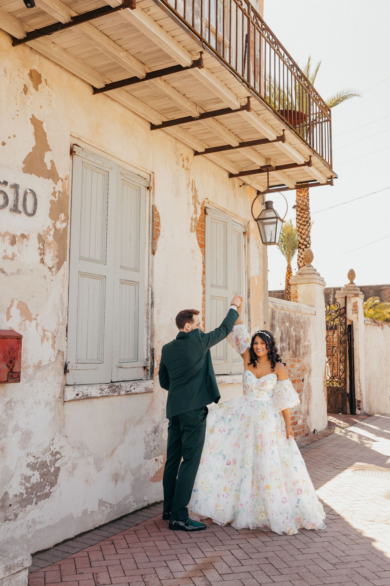 A couple shares a romantic moment outside a historic building with weathered walls and iron balcony at Race and Religious in New Orleans
