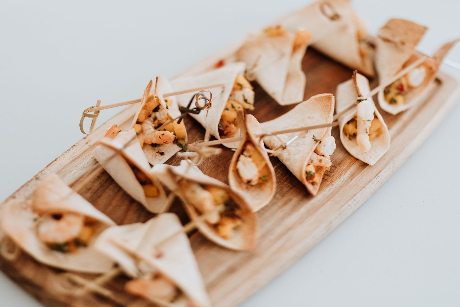 Small tortilla wraps filled with savory ingredients arranged on a wooden serving board.