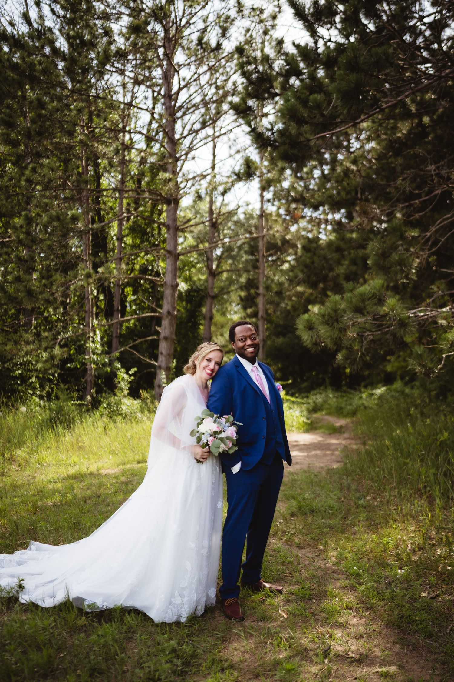 Wedding couple walking and posing together on a wooded nature trail surrounded by tall pine trees.