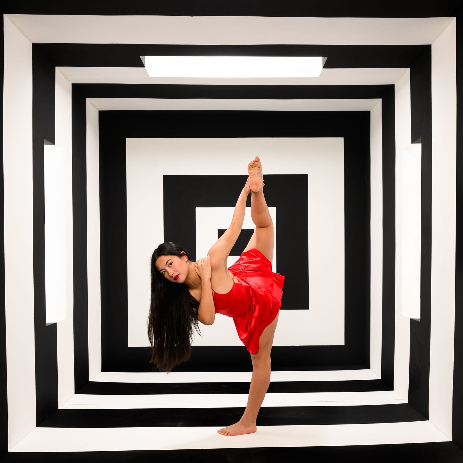Graceful dancer performs against geometric black and white pattern background.