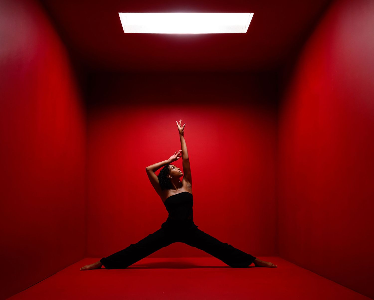 Dynamic dancer silhouette performs expressive movements against red-walled studio with stark lighting.