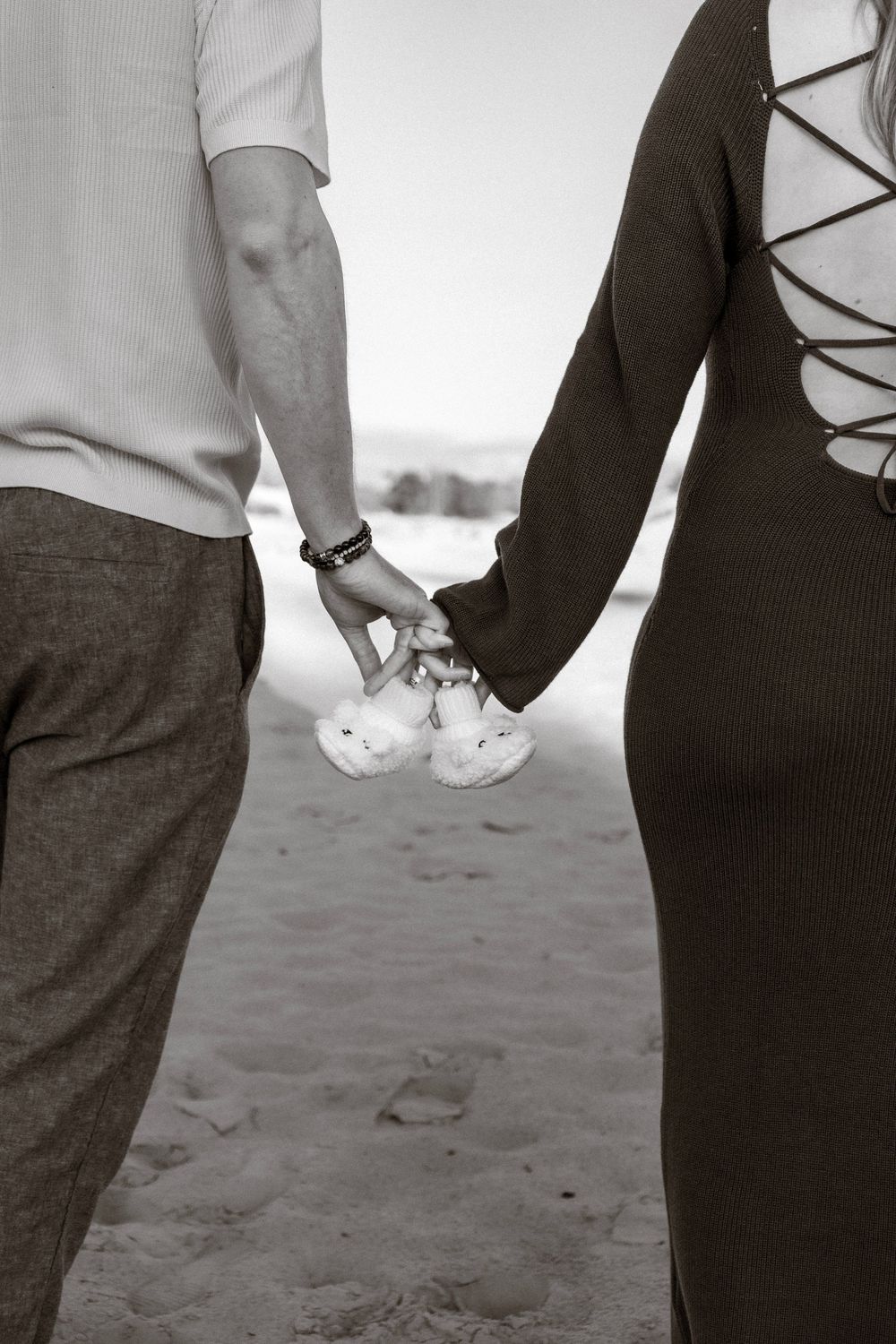 Zwart-witfoto van een stel dat hand in hand op het strand staat, met babyschoentjes tussen hen in.