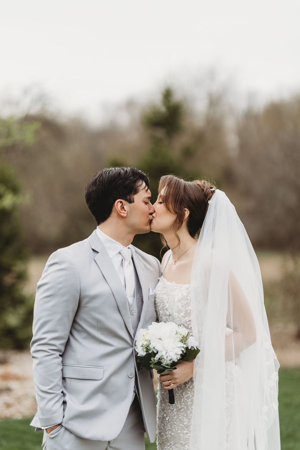 A romantic wedding portrait shows a couple sharing a kiss outdoors, with the bride in a lace gown and flowing veil.