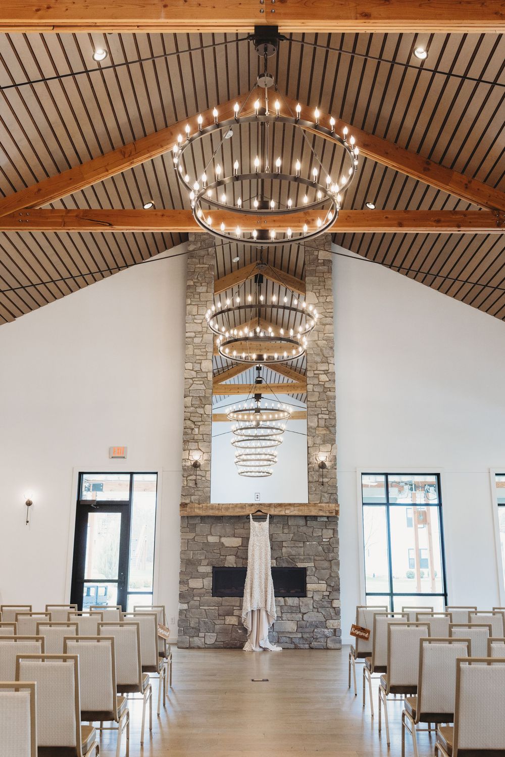A modern chapel interior with circular chandeliers, stone fireplace, and white chairs arranged in rows for a ceremony.