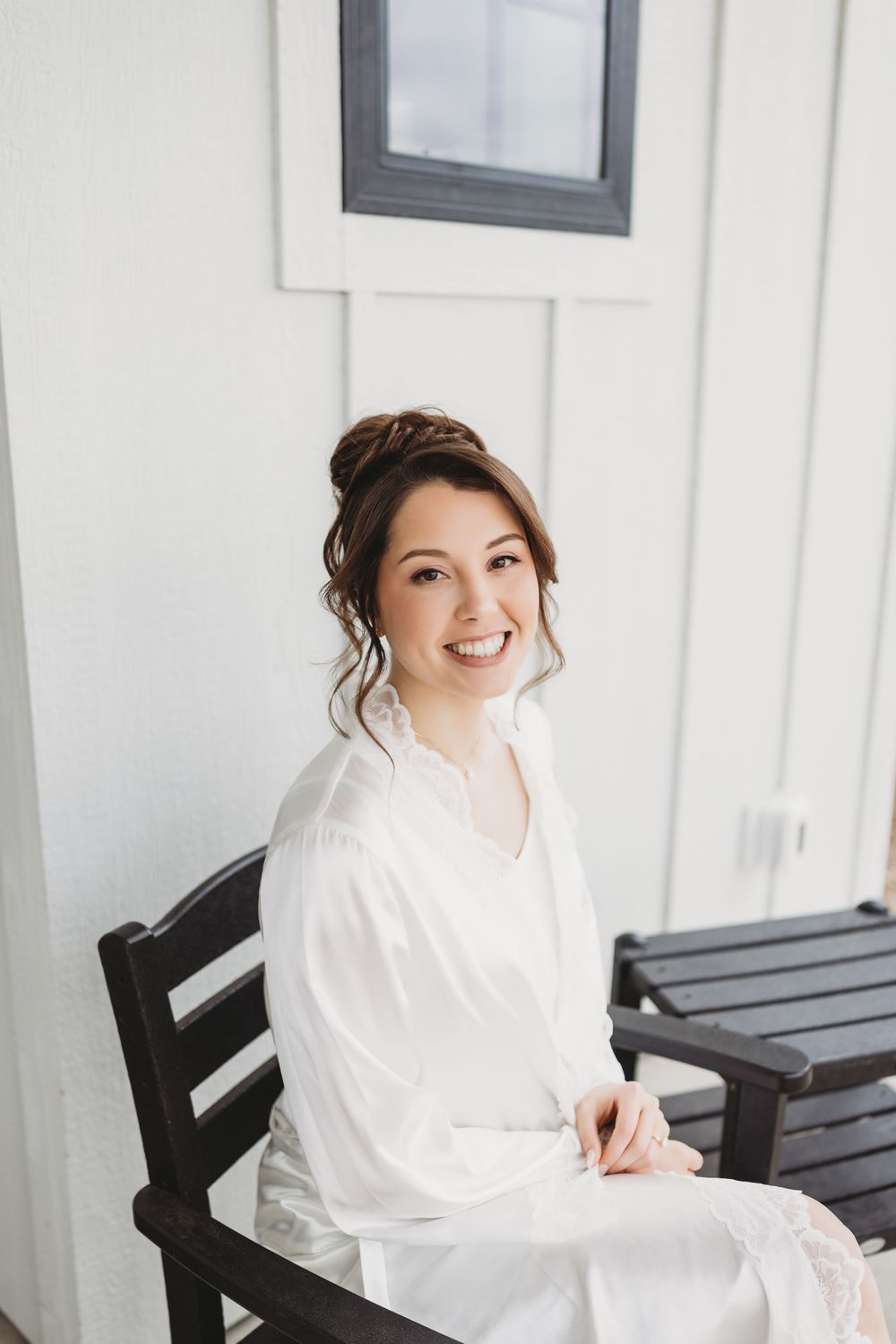 A smiling woman in a white robe sits gracefully on a dark wooden bench.