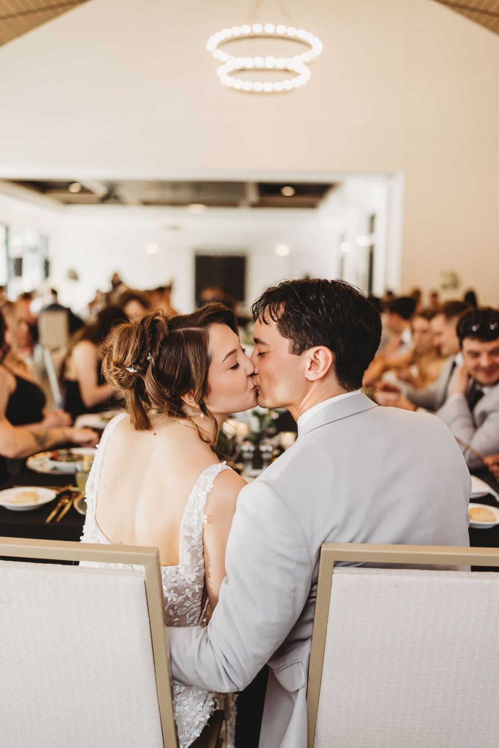 A romantic wedding reception moment with a newlywed couple sharing a kiss at their table under elegant lighting.