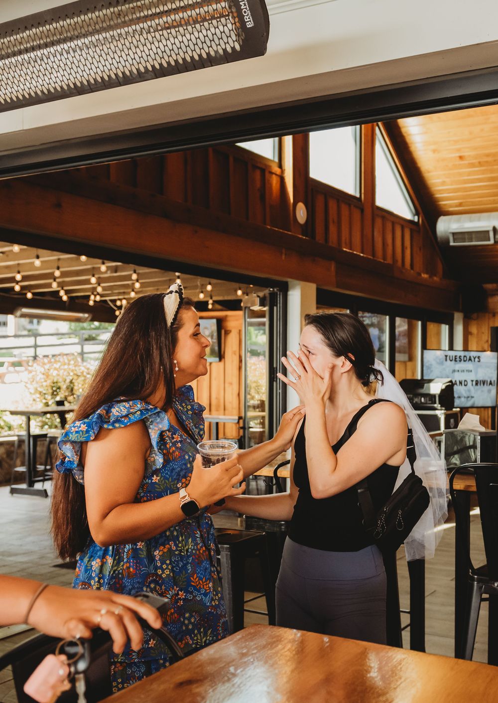Two excited friends celebrating a special moment together at a rustic restaurant with wooden beams and warm lighting.