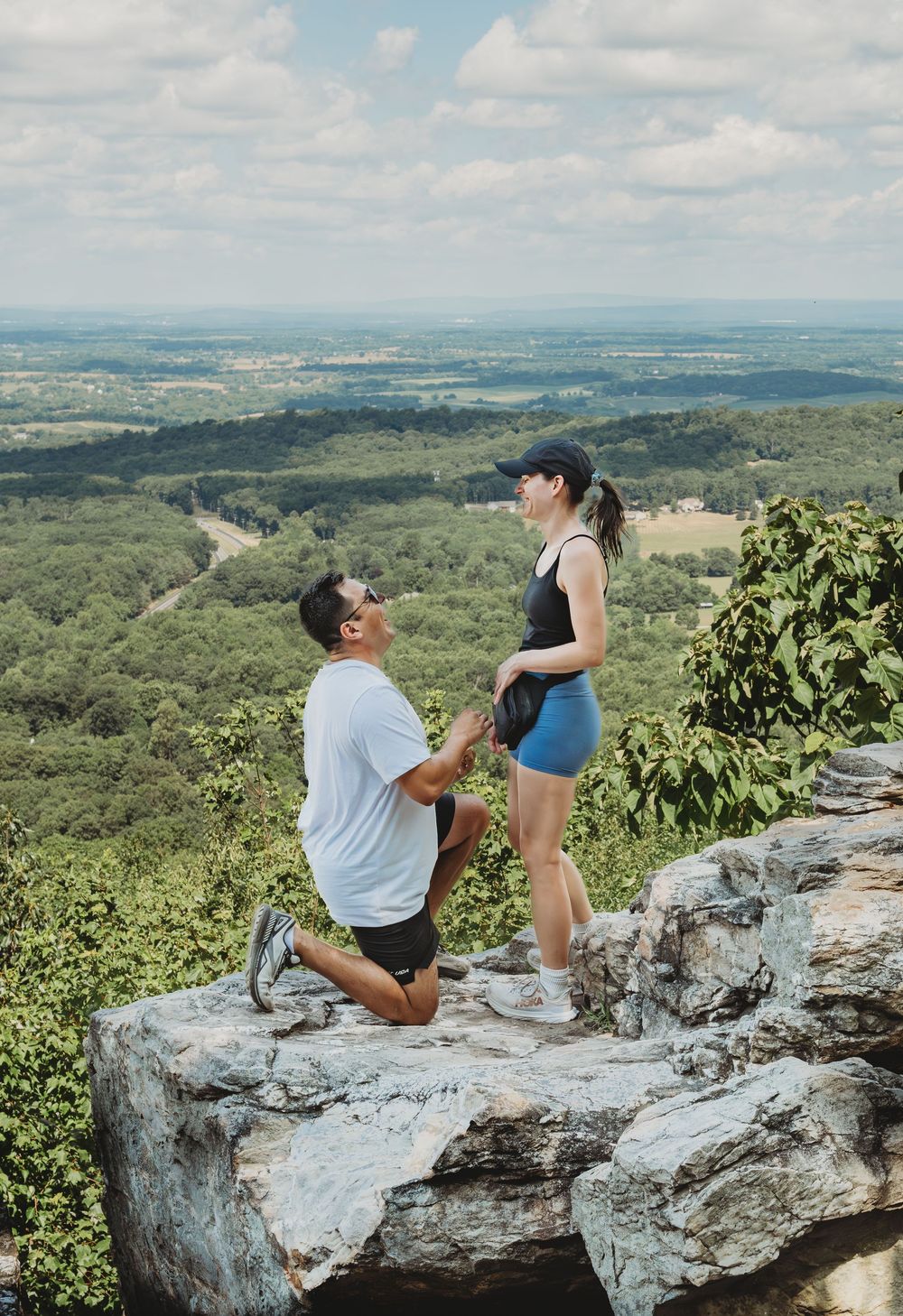 A couple share a special moment at a scenic mountain overlook with rolling hills and valleys stretching into the distance.