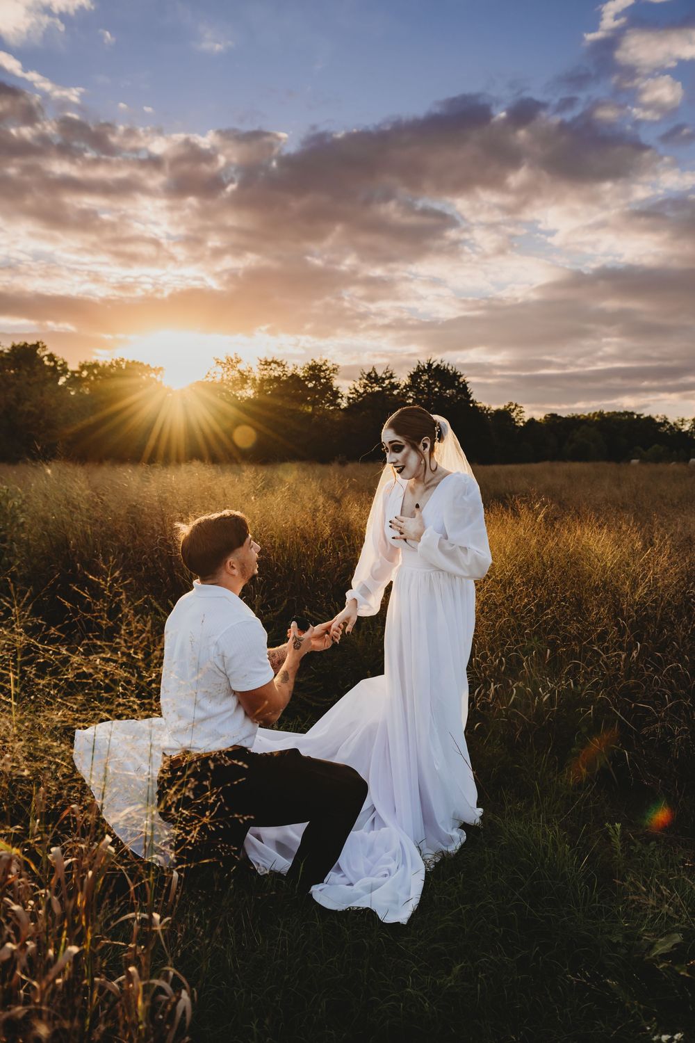 A romantic sunset engagement moment in a golden field with dramatic clouds and sunburst in the background.