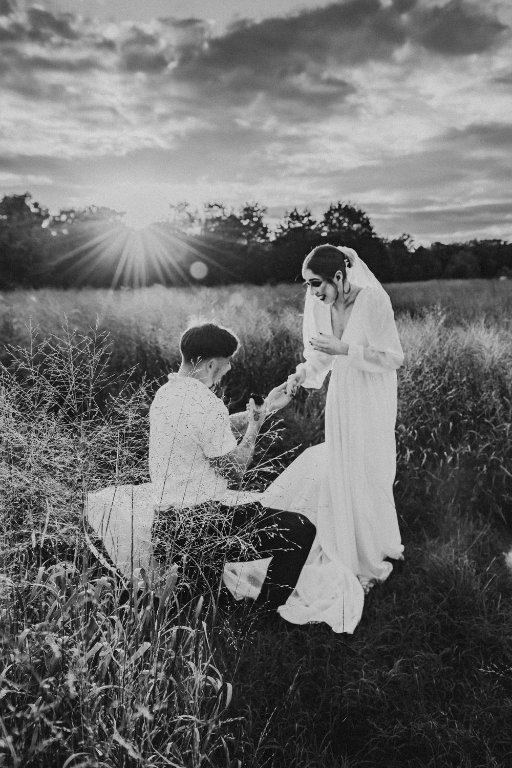 A romantic proposal scene in a sun-drenched meadow at sunset, with dramatic sunburst in black and white.