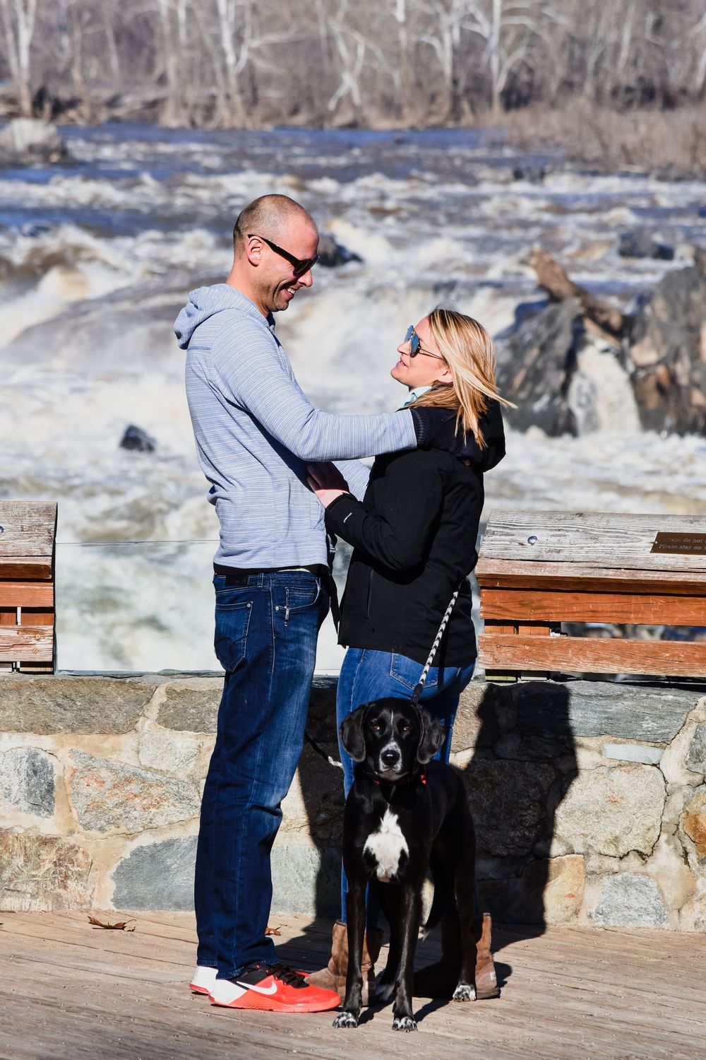 A couple shares a romantic moment on an observation deck overlooking a scenic river with rapids.