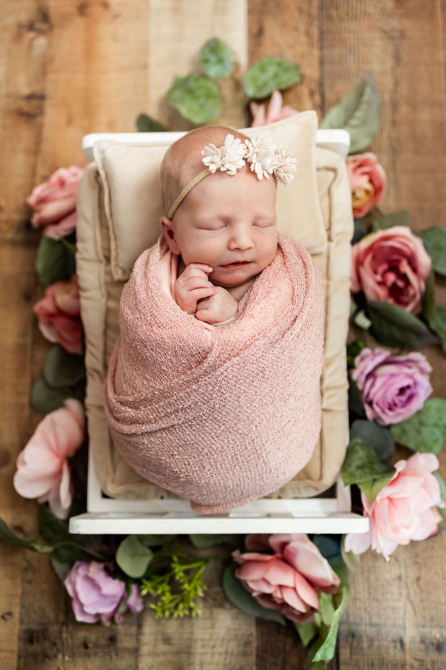 Sleeping newborn wrapped in pink swaddle lying in white wooden box surrounded by pink and purple roses. Newborn Photographer in Richmond, VA