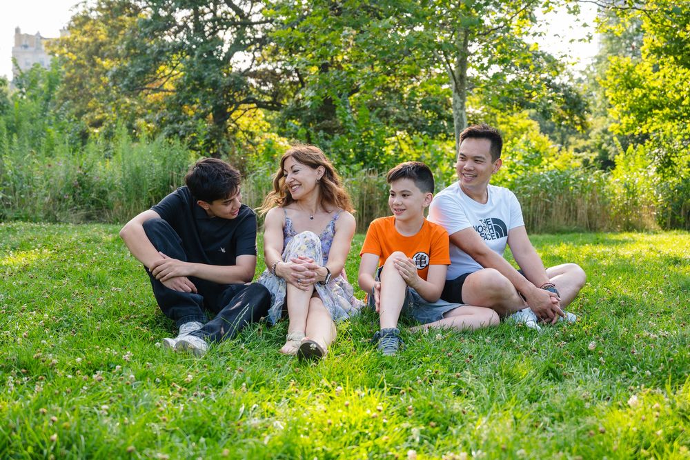 A family relaxing together on grassy hill during golden hour in summer park setting.