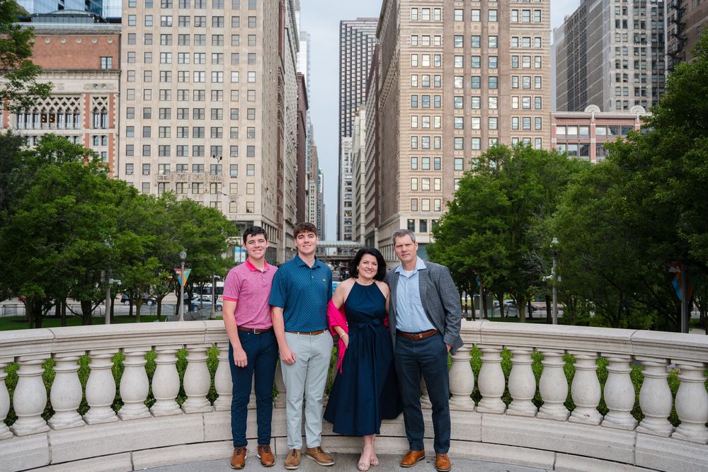 A family stands on a balcony overlooking a tree-lined city street with historic buildings in Chicago.